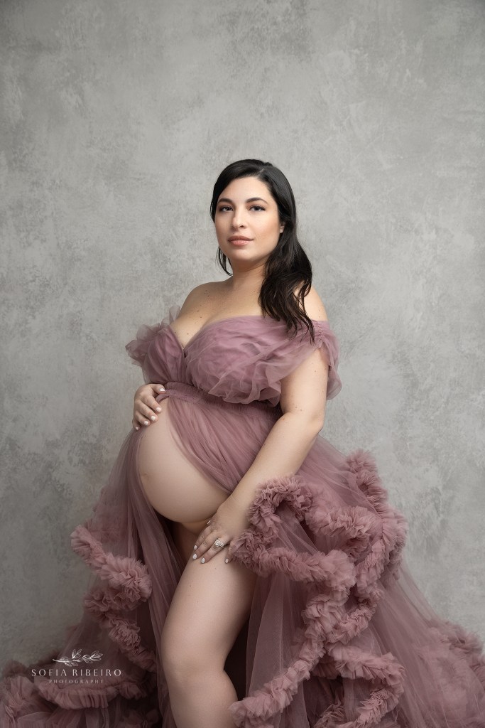 mom poses while showing her belly, looking into the camera during a maternity session