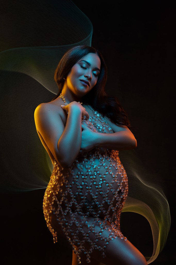 a blue gel light highlights moms face and belly, while two orange side lights outline her curves during a maternity photo session in a jersey city nj maternity portrait studio