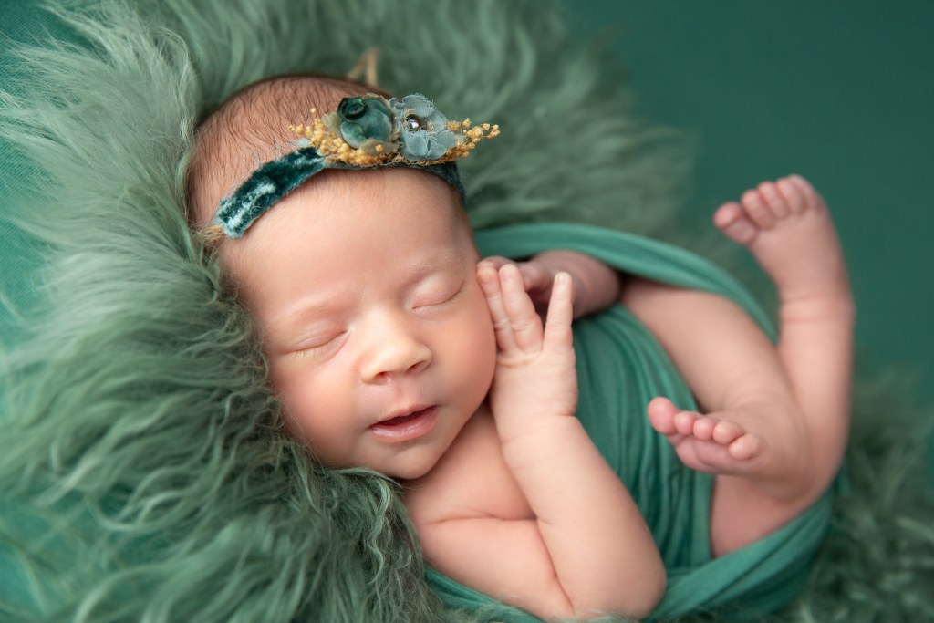 baby girl smiles while wearing green during a newborn session
