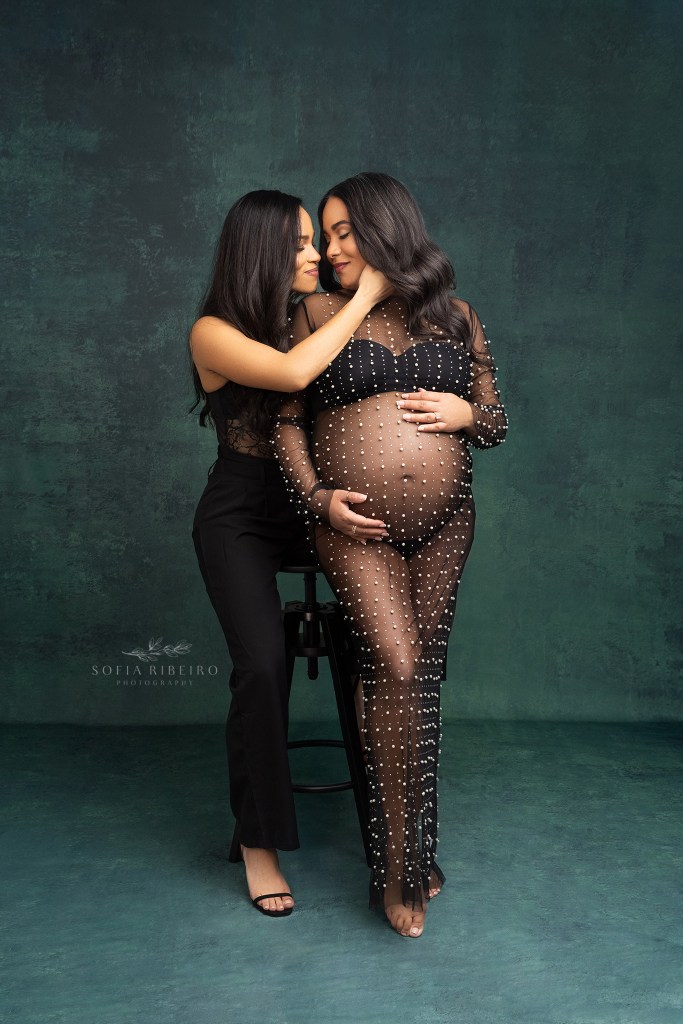 two moms pose together in black outfits, holding the expectant moms belly and face lovingly during a jersey city nj maternity session