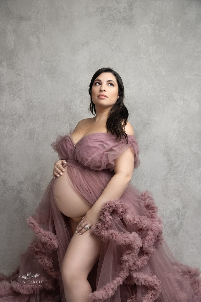 mom poses while showing her belly, looking into the key light during a maternity session