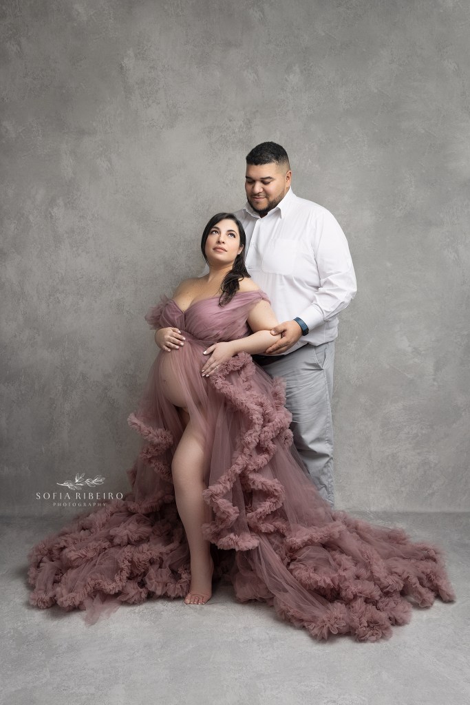 dad looks lovingly at expectant mom in a pink maternity gown for photos