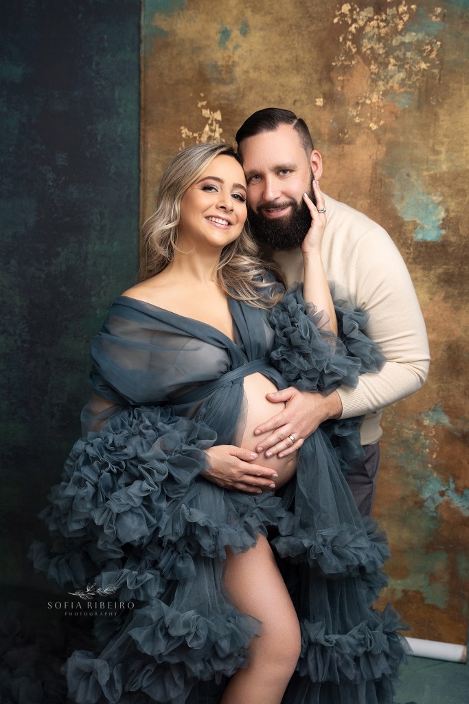 mom poses in a teal ruffled robe with her husband during a photo session with a clark nj maternity photographer
