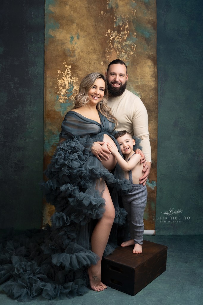 mom poses in a teal ruffled robe with her family during a photo session with a clark nj maternity photographer