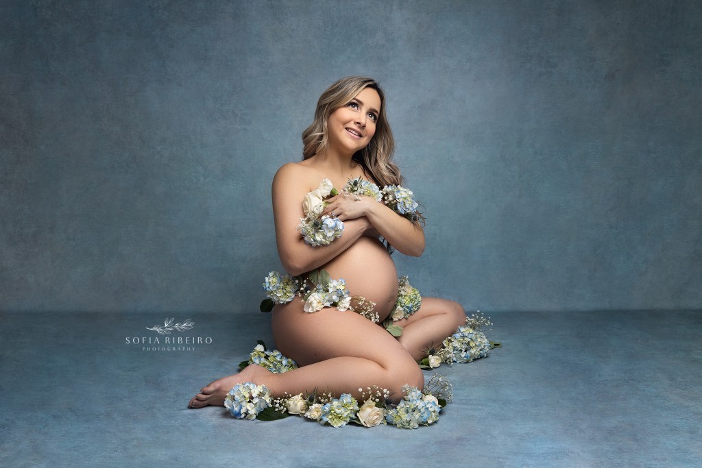 mom poses with flowers covering her belly in blue fabric during a photography session celebrating her pregnancy