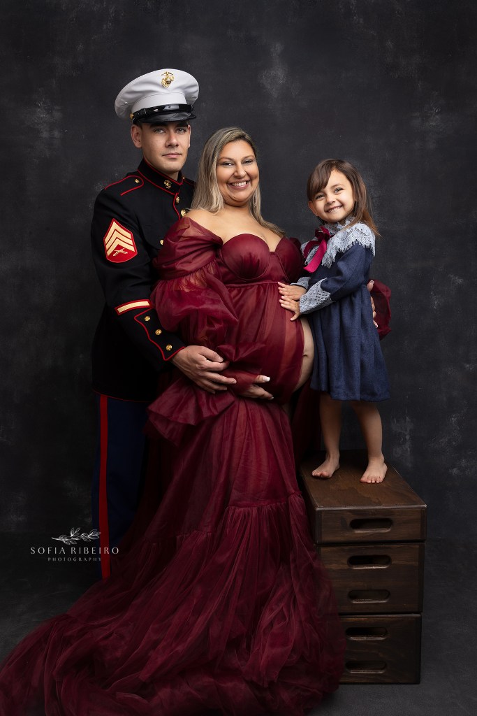 mom poses with family and dad in dress blues during a maternity session with nj maternity photographer in roselle park nj