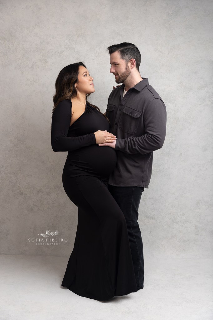 dad and mom face each other with hands on belly, lovingly posing