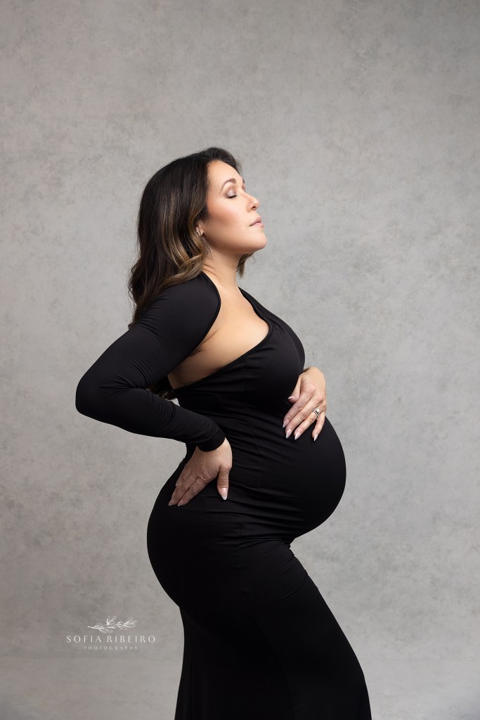 mom poses with hands on belly in a black dress during a nj maternity session