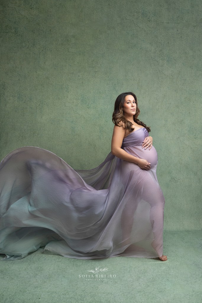 mom poses in billowing purple fabric against a sage background during a photo session for maternity in nj