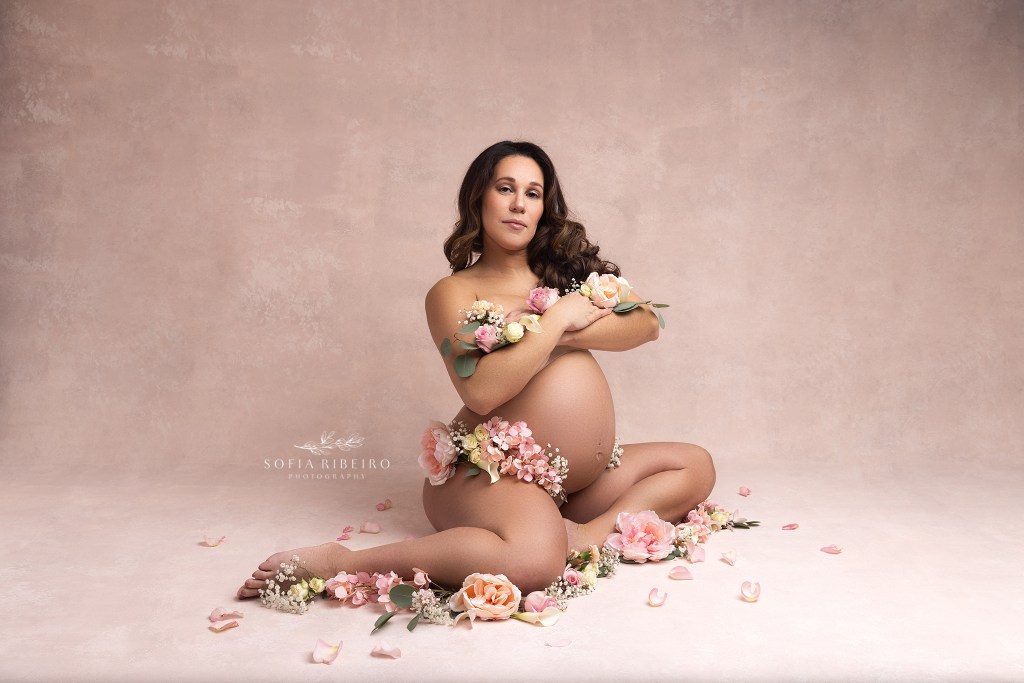 mom poses nude, with arms crossed in front of her, draped in flower highlighting her belly during a nj maternity session