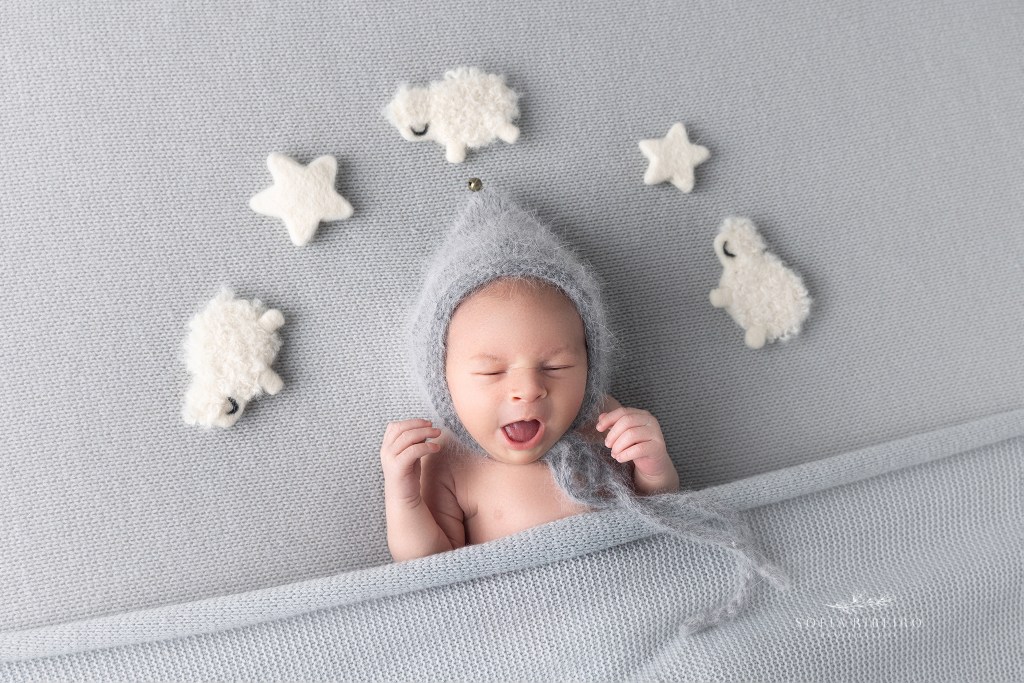 baby yawns quietly sleeping on a grey backdrop and counting sheep above his head