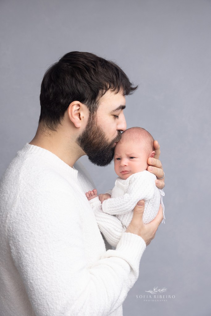 dad holds his baby close to his chest and gives him a kiss during a newborn session