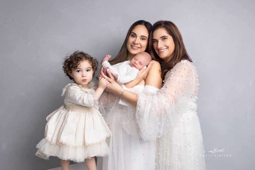 grandma hugs her daughter who is holding her new baby and big sister during baby's newborn session