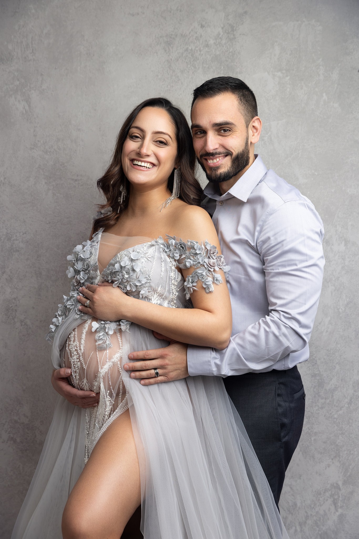 Happy expecting parents stand in a studio holding the bump before needing pelvic floor therapy nj