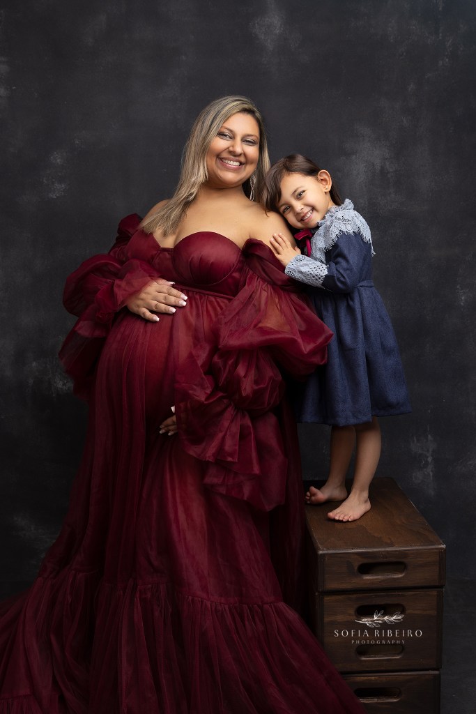 mom poses with toddler daughter in a red dress during a maternity session in roselle park nj