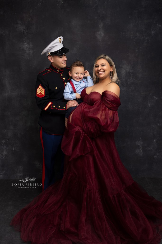 mom poses with family and dad in dress blues during a maternity session with nj maternity photographer in roselle park nj