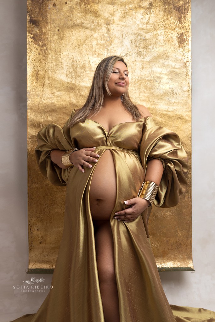 mom cradles her belly wearing a gold dress and headpiece in between photos during her nj maternity photo session