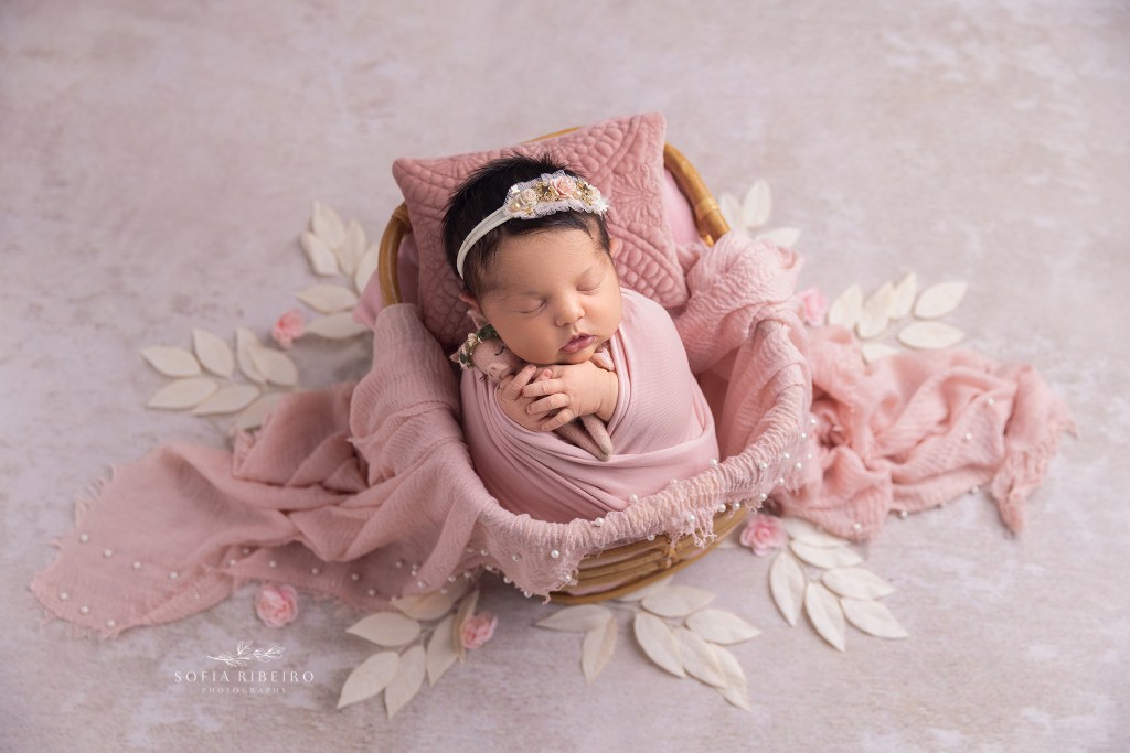 a baby girl is posed in a basket surrounded by pink and white florals during a photo session