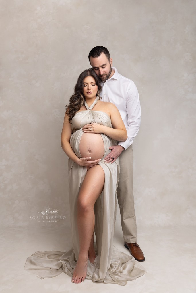 mom and dad pose lovingly cradling moms bump, while draped in cream fabric during a session with dover nj maternity photographer