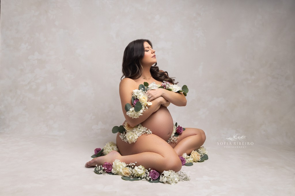 mom poses on the floor draped in roses and other foliage highlighting her baby bump