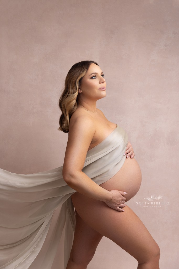 mom is draped in a billowing cream silk fabric, with baby bump exposed during a maternity photo session in garwood nj
