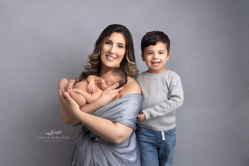 mom beams with pride, holding her newborn and older son during a photo session with a garwood nj newborn photographer
