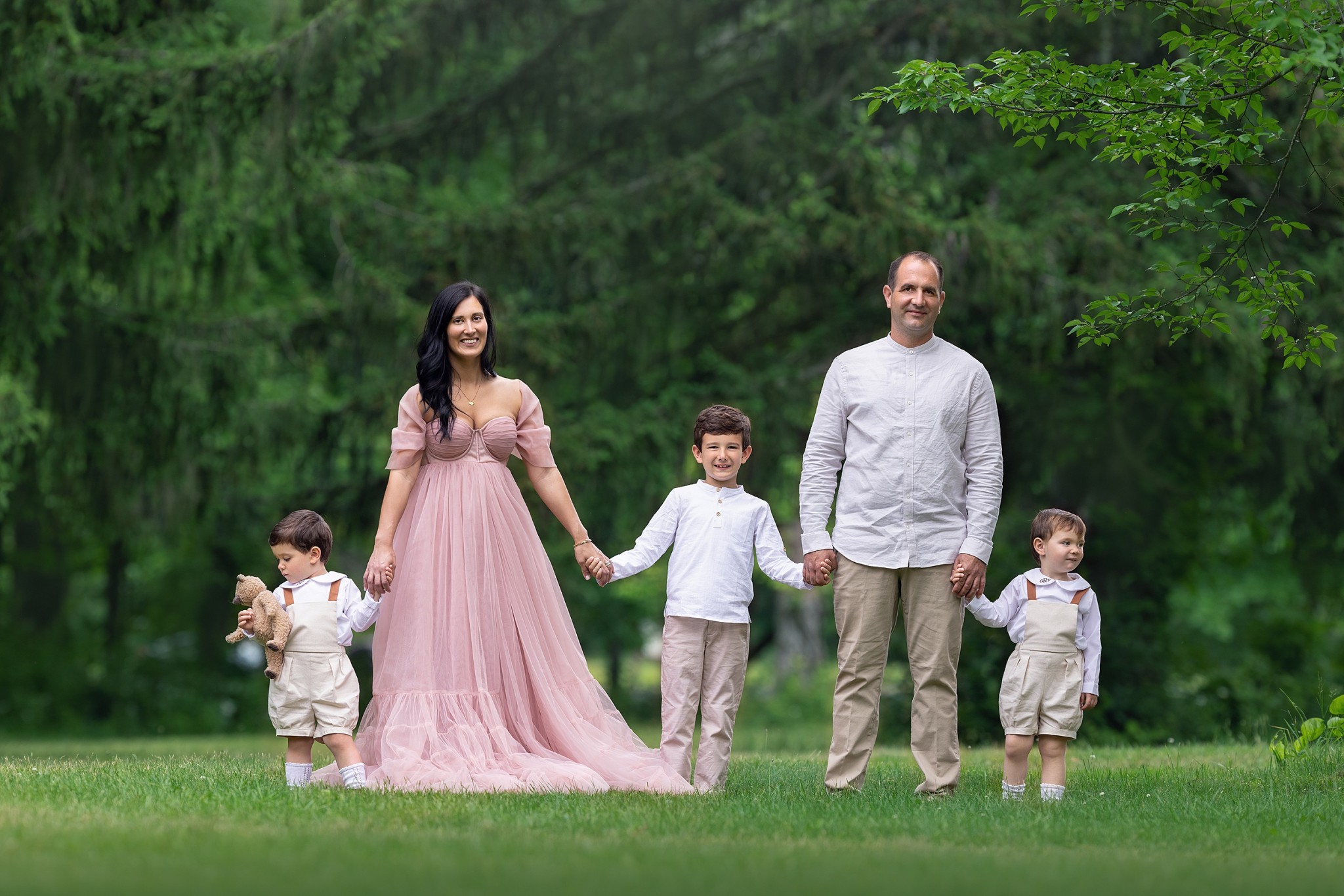 A mom and dad stand in a green lawn holding hands with their three toddler sons before visiting montessori schools nj