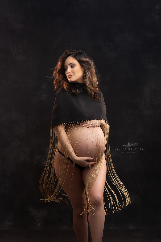 mom's baby bump is silhouetted against a blank background and gold flowing fringe during maternity photos in red bank nj