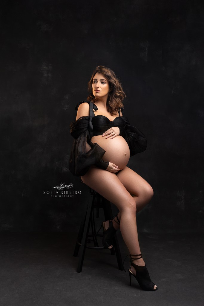 mom poses, seated, with a tulle black top during a maternity session