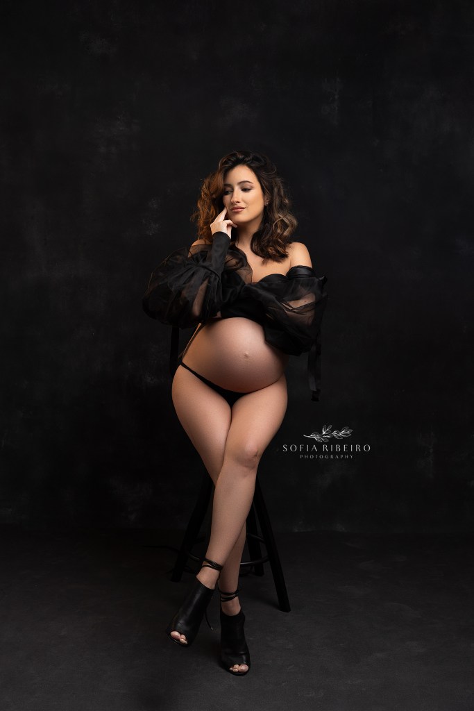 mom poses, seated, with a tulle black top during a maternity session