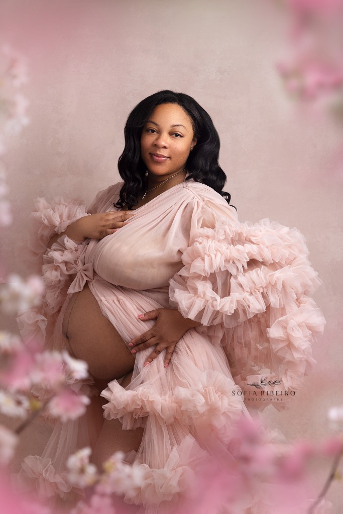 mom poses in blossoms in pink during a maternity session in orange nj