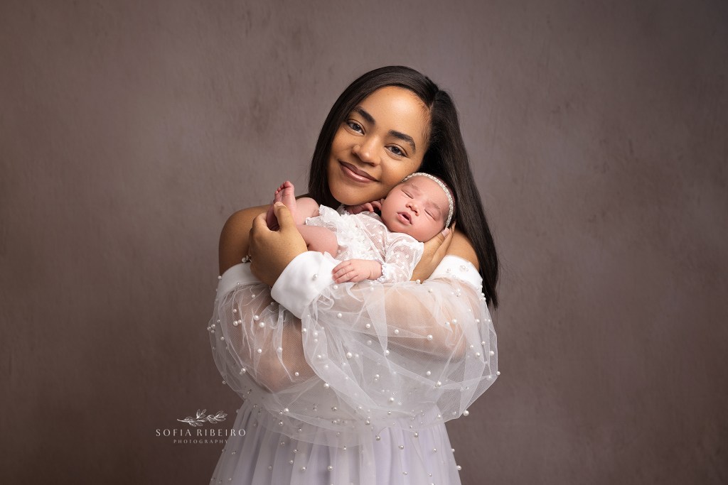 mom snuggles baby in a pearl dress against a brown backdrop during a newborn session with a randolph nj newborn photographer