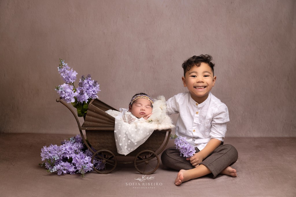 big brother smiles big with his new baby sister in a carriage prop during a session with a randolph nj newborn photographer