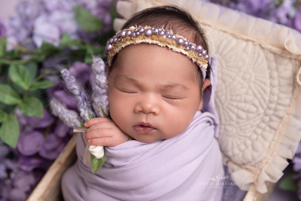 little bayb holds a sprig of lavender while wrapped in a purple wrap during a newborn session