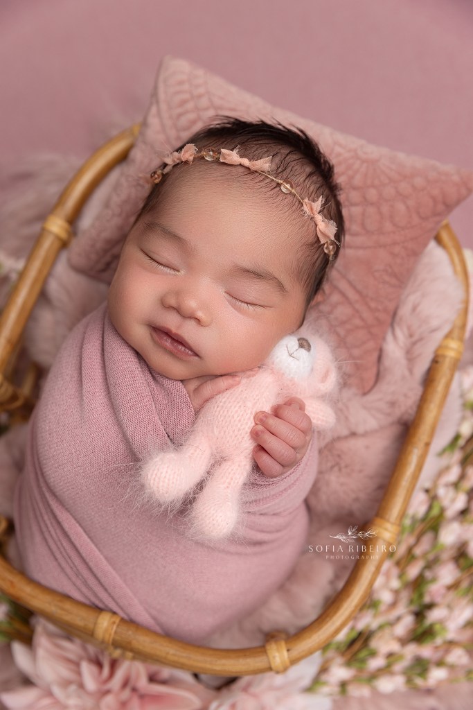 newborn girl smiles while hugging a stuffed pink teddy bear during a photo session in randolph nj