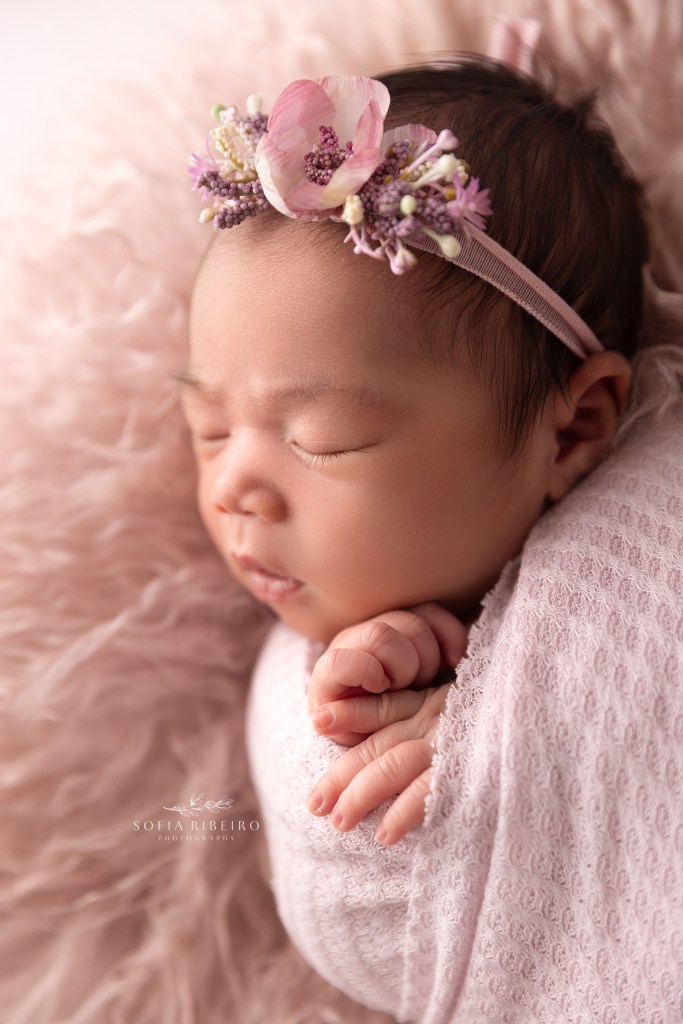 little girl sleeps sweetly wrapped in pink with a floral headband during a newborn session in randolph nj
