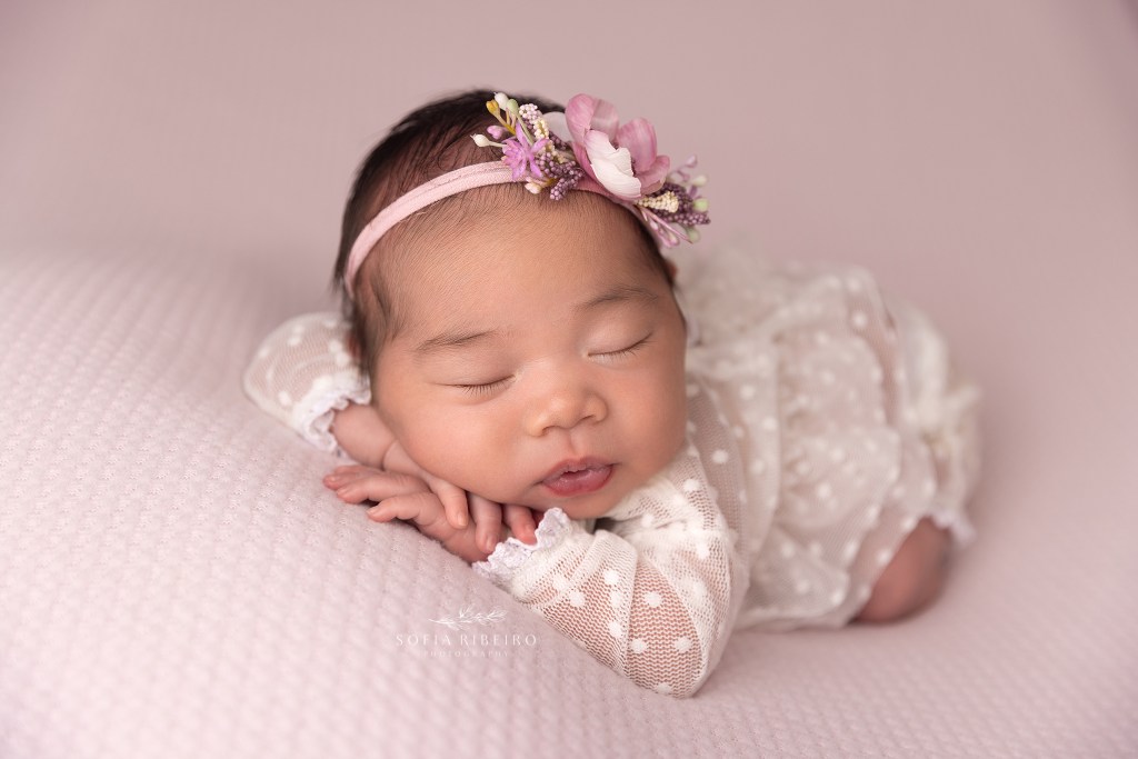 little girl sleeps sweetly wrapped in pink with a floral headband during a newborn session in randolph nj