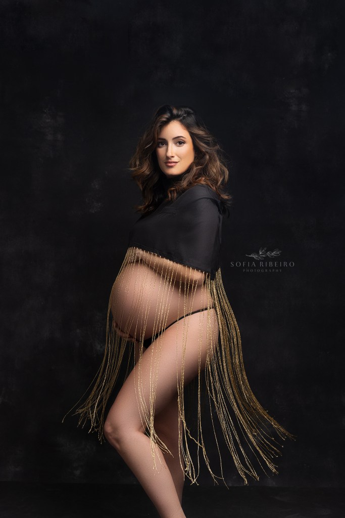 mom's baby bump is silhouetted against a blank background and gold flowing fringe during maternity photos in red bank nj
