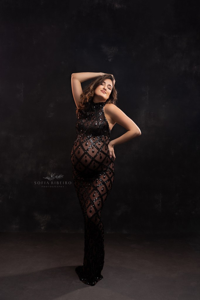 mom strikes a pose in an elegant black beaded dress highlighting her baby bunmp during a maternity session in nj