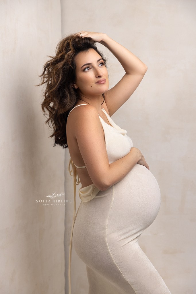 mom wearing a cream dress poses, tousling her hair during a session with a red bank maternity photographer
