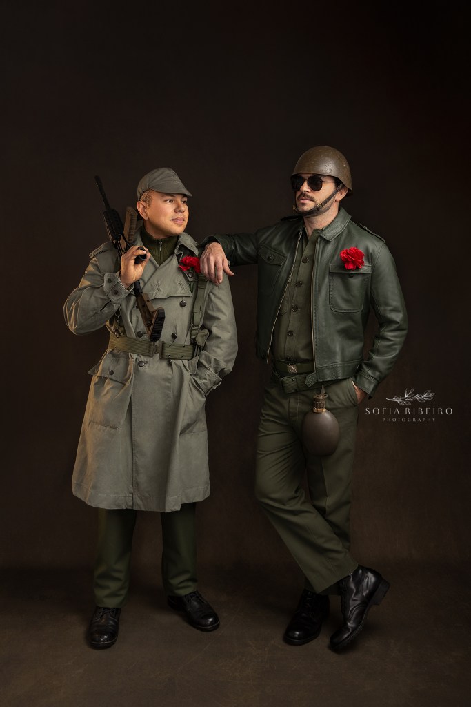 two styled soldiers in portuguese military uniforms from the 70s, with carnations in lapels, pose for a photo celebrating the 50th anniversary of portugal's carnation revolution. dois modelos posam como soldados dos anos 70 em portugal, com cravos nos casacos, em comemoracao dos eventos da revolucao do dia 25 de abril