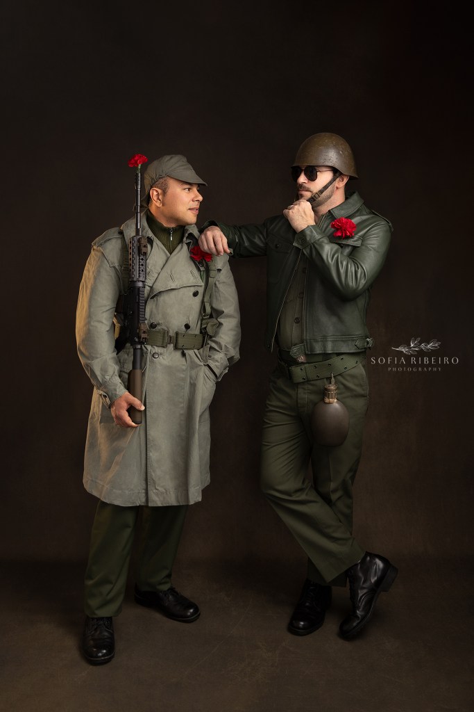 two styled soldiers in portuguese military uniforms from the 70s, with carnations in lapels, pose for a photo celebrating the 50th anniversary of portugal's carnation revolution. dois modelos posam como soldados dos anos 70 em portugal, com cravos nos casacos, em comemoracao dos eventos da revolucao do dia 25 de abril