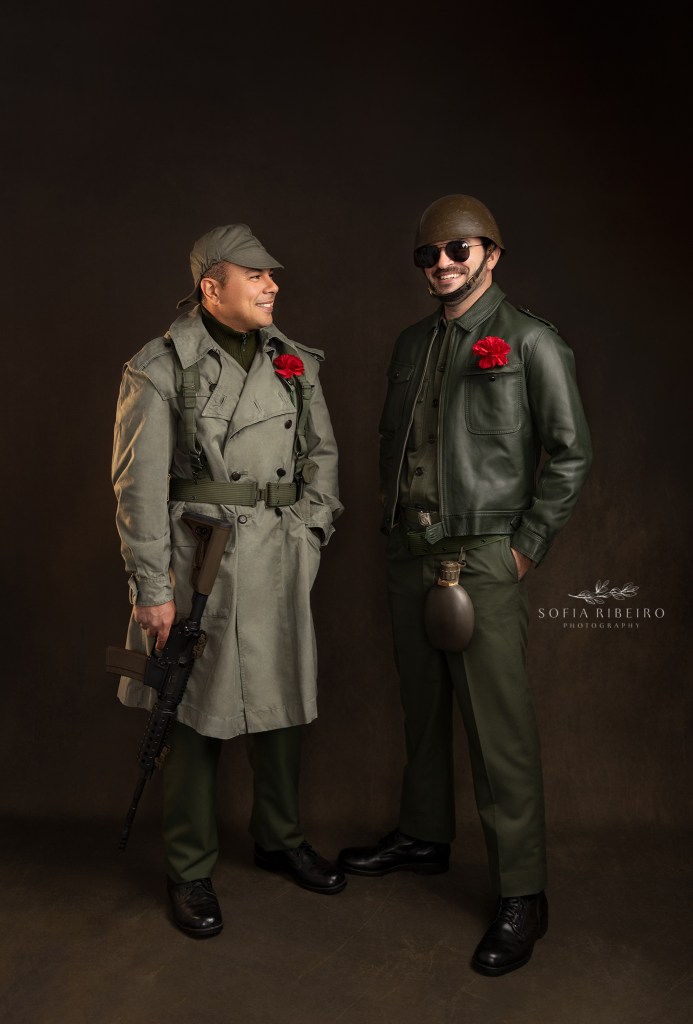two styled soldiers in portuguese military uniforms from the 70s, with carnations in lapels, pose for a photo celebrating the 50th anniversary of portugal's carnation revolution. dois modelos posam como soldados dos anos 70 em portugal, com cravos nos casacos, em comemoracao dos eventos da revolucao do dia 25 de abril