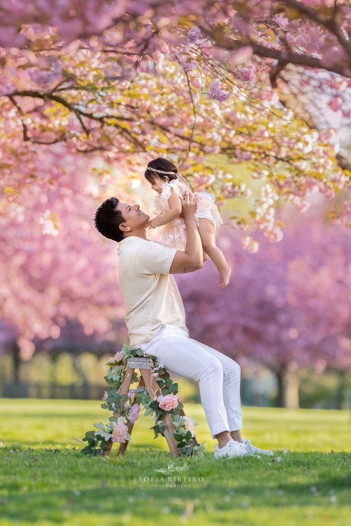 dad tosses baby in air playfully during their cherry blossom session in nj