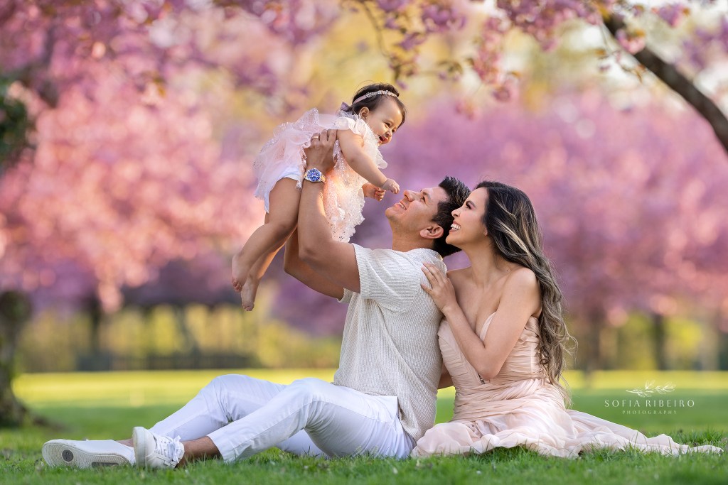 dad and mom play in the grass with their baby girl in matching outfits during cherry blossom season in nj