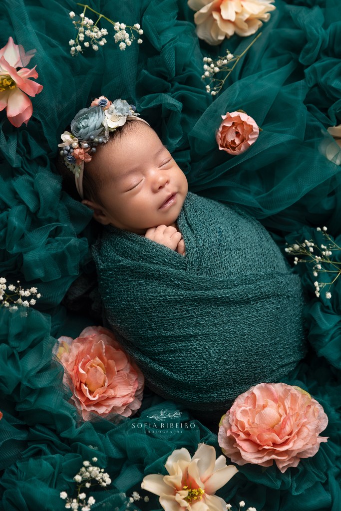 baby girl is posed in green ruffles with peach flowers scattered around during a session with englewood nj newborn photographer