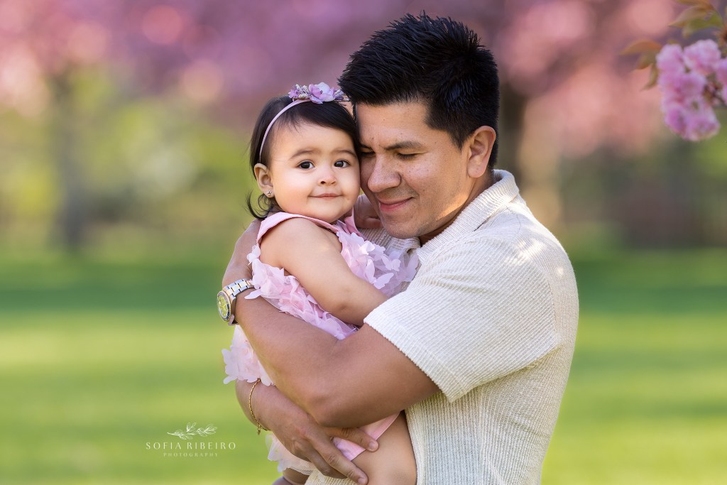 dad snnuggles his baby girl with cherry trees in the background