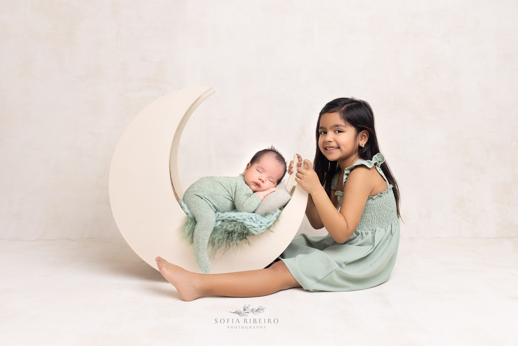 baby brother sleeps soundly on a prop moon while big smiles sweetly at the camera