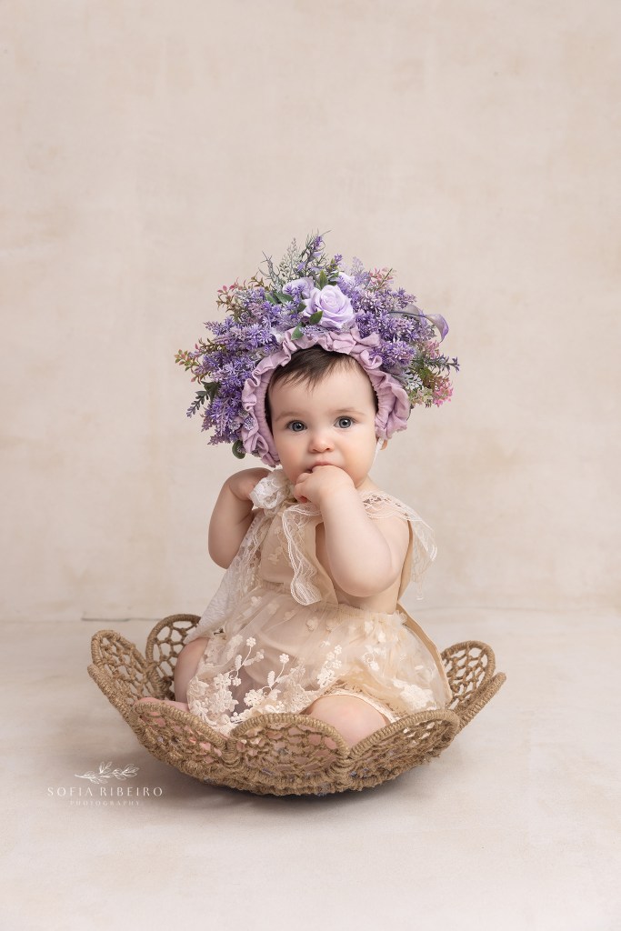 baby sits in a bowl with a cream romper and purple headress in westfield nj