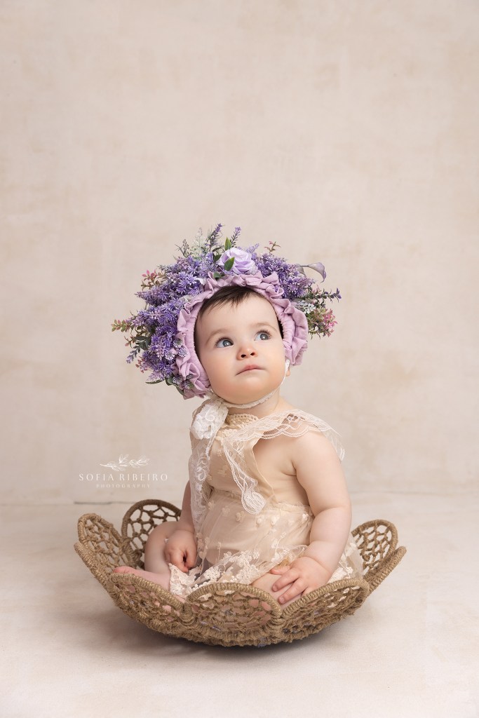 baby sits in a bowl with a cream romper and purple headress in westfield nj